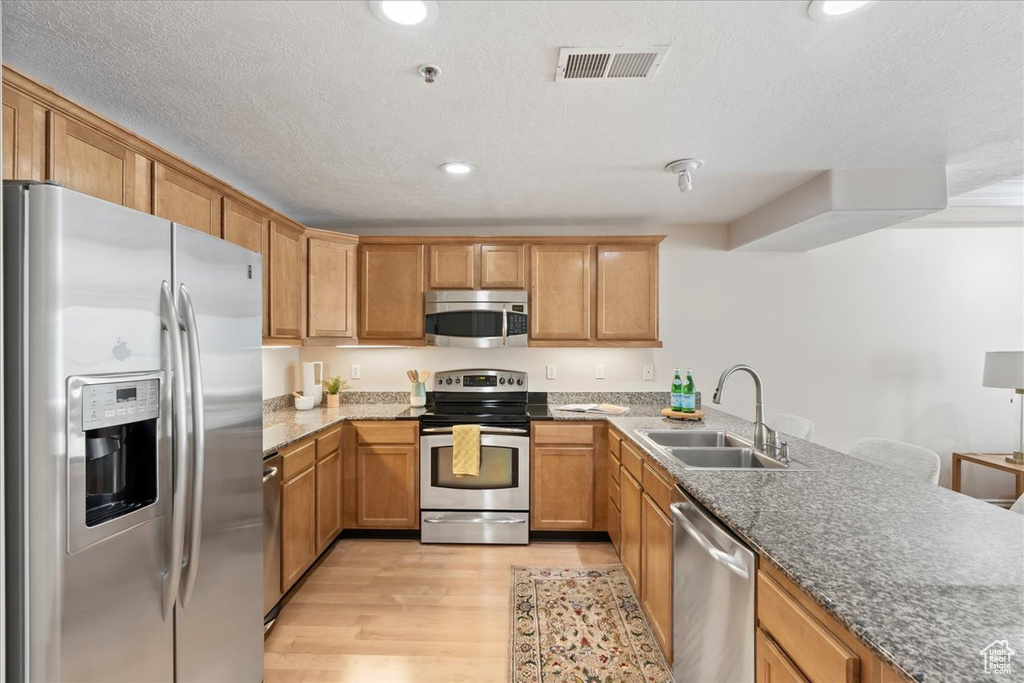 Kitchen featuring appliances with stainless steel finishes, a sink, light wood finished floors, dark stone countertops, and recessed lighting