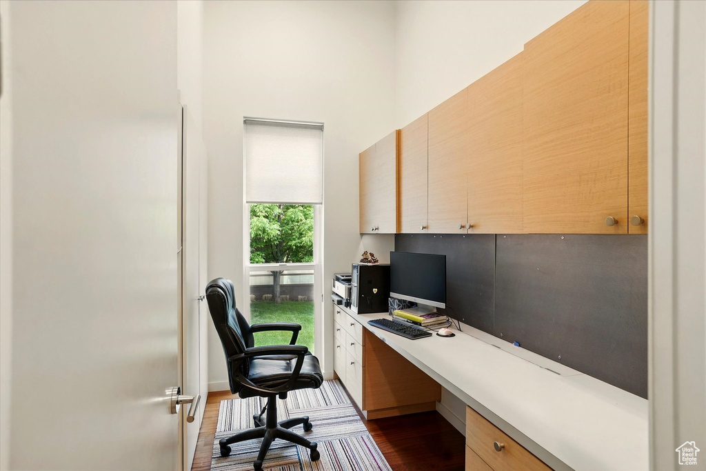 Office area featuring dark wood finished floors, built in study area, and a towering ceiling