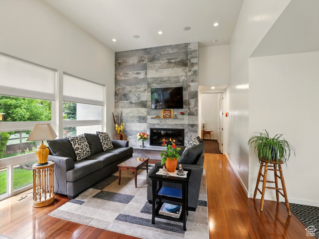 Living area with hardwood / wood-style floors, a tile fireplace, baseboards, recessed lighting, and a high ceiling