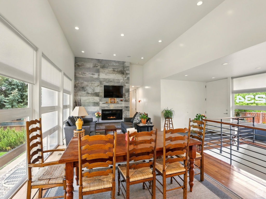 Dining room with recessed lighting, wood finished floors, a tiled fireplace, and a high ceiling