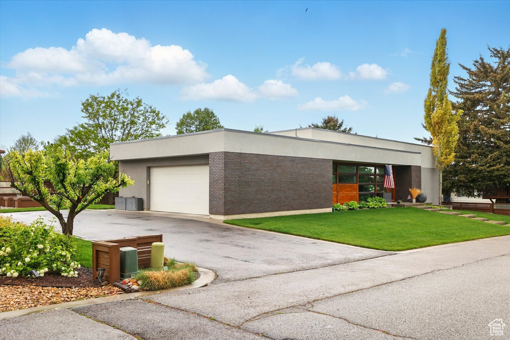 View of front facade with an attached garage, driveway, a front yard, and stucco siding