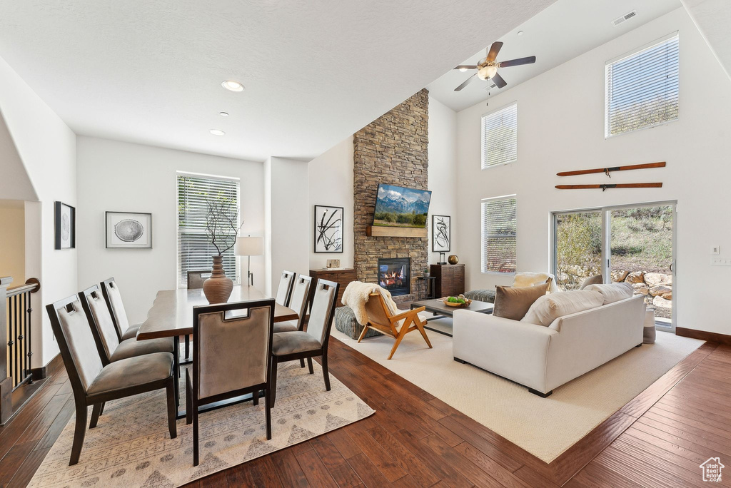 Dining room with dark wood-type flooring, ceiling fan, a stone fireplace, baseboards, and high vaulted ceiling