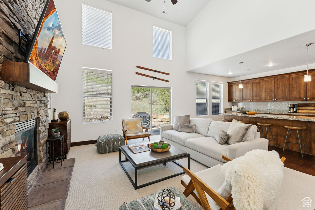Living room featuring a ceiling fan, a high ceiling, baseboards, and a fireplace