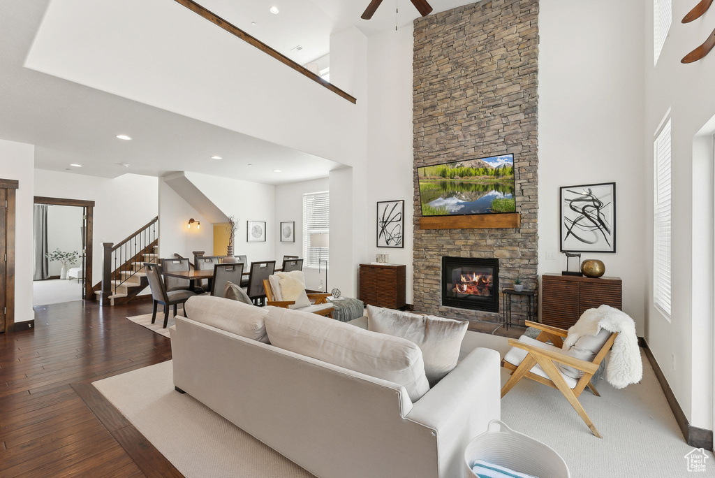 Living room featuring ceiling fan, a high ceiling, a fireplace, dark wood-type flooring, and stairway