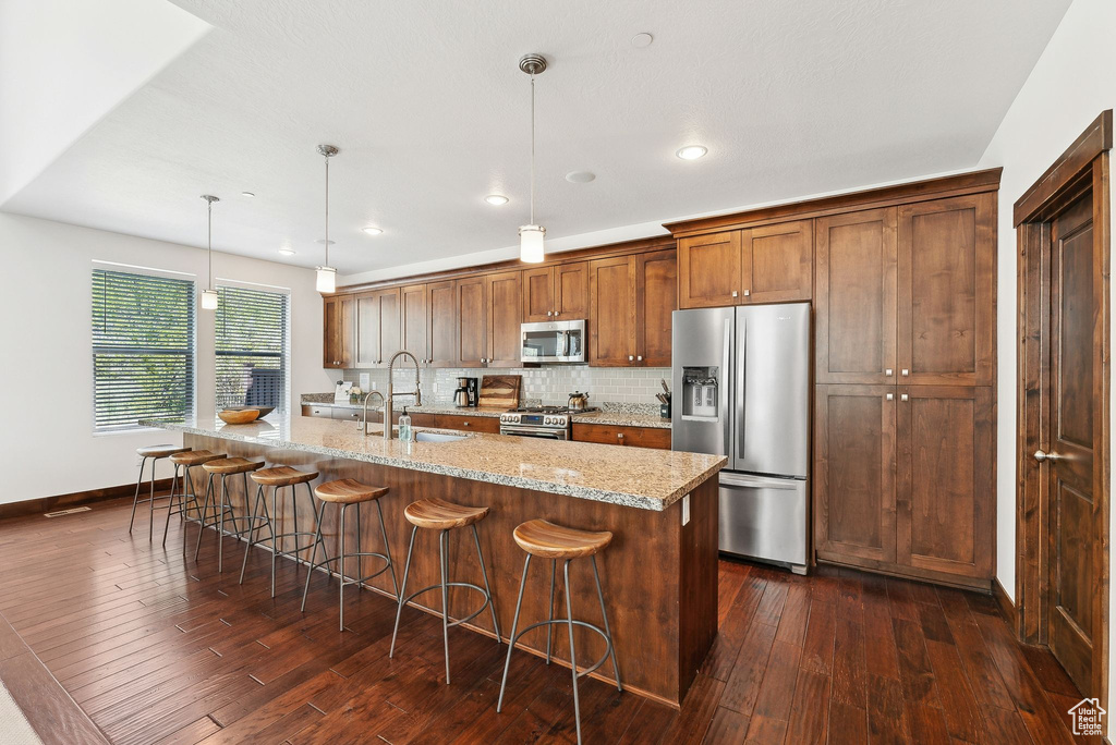 Kitchen with stainless steel appliances, a sink, dark wood finished floors, backsplash, and an island with sink