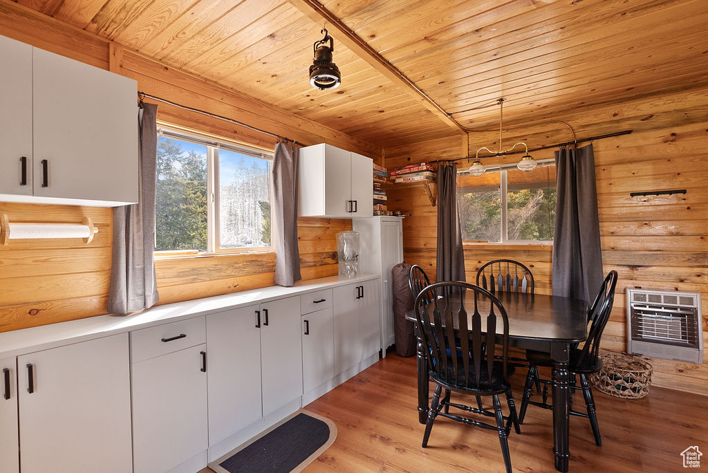 Dining area featuring heating unit, healthy amount of natural light, wood ceiling, light wood-type flooring, and wood walls