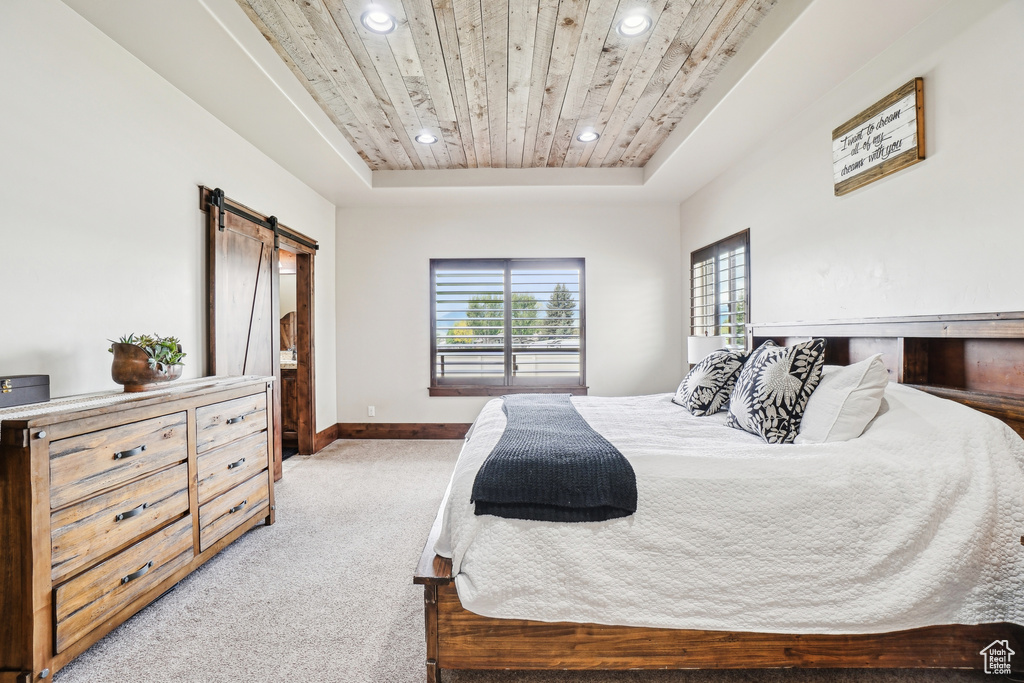 Bedroom with a barn door, a raised ceiling, light carpet, wooden ceiling, and recessed lighting