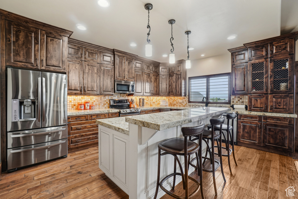 Kitchen featuring appliances with stainless steel finishes, a center island, light wood-style flooring, backsplash, and recessed lighting