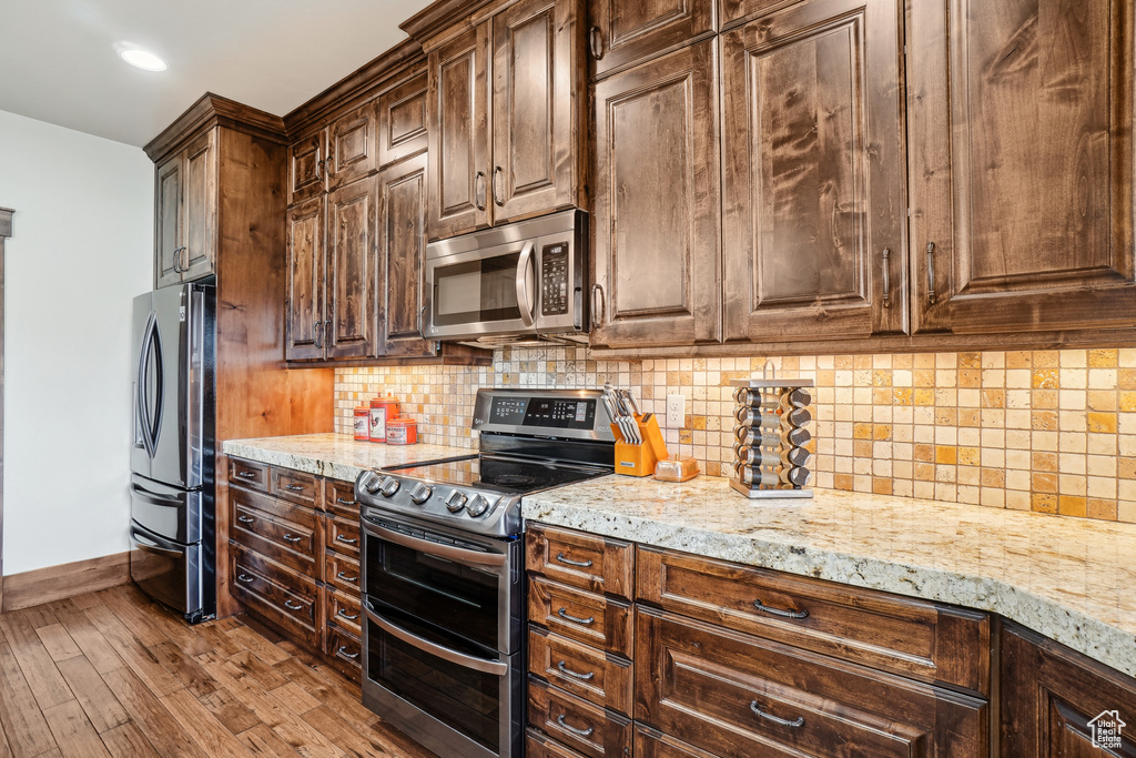 Kitchen featuring stainless steel appliances, baseboards, light stone counters, wood finished floors, and tasteful backsplash