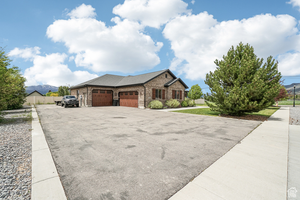 View of front of house with an attached garage, asphalt driveway, brick siding, fence, and roof with shingles