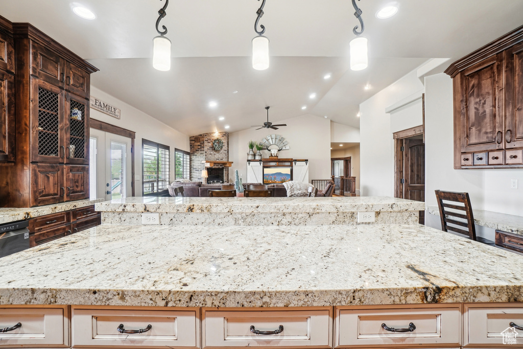 Kitchen featuring ceiling fan, lofted ceiling, open floor plan, a large fireplace, and light stone counters