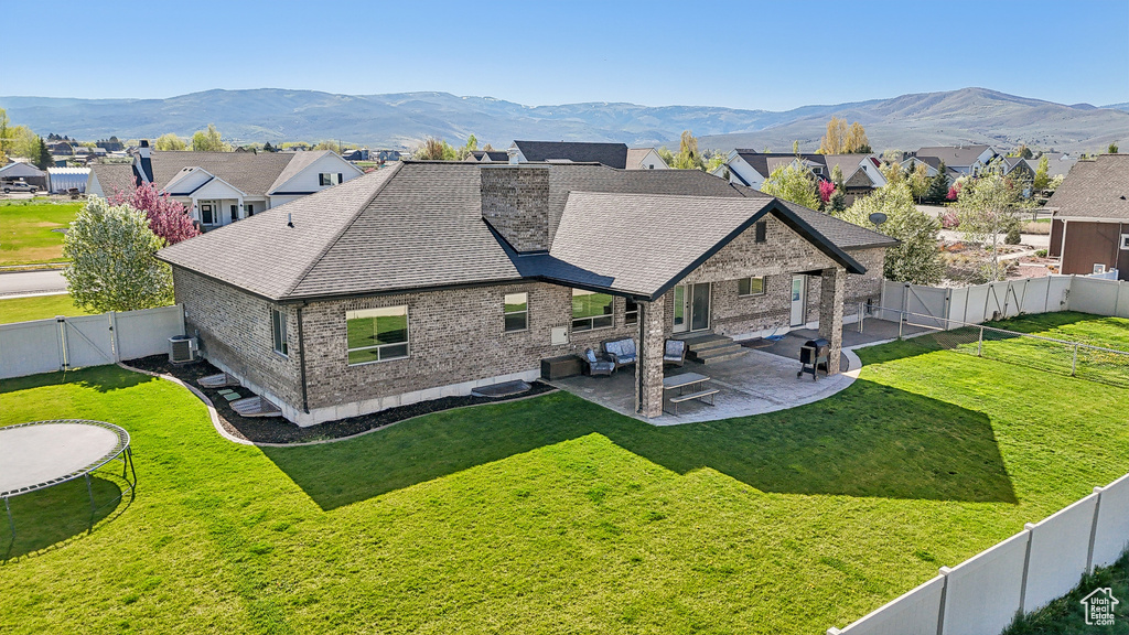 Back of property featuring a trampoline, a patio, a shingled roof, a gate, and brick siding