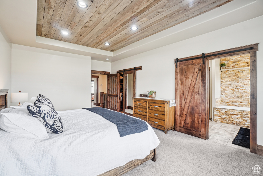 Carpeted bedroom with a barn door, wood ceiling, recessed lighting, a tray ceiling, and ensuite bath