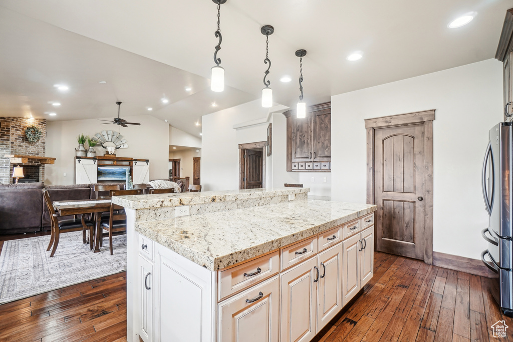 Kitchen featuring freestanding refrigerator, a ceiling fan, dark wood-style flooring, light stone countertops, and a kitchen island