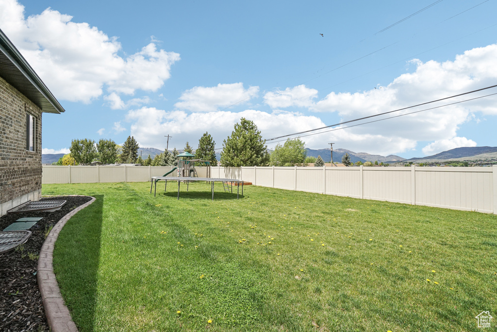 View of yard with a trampoline, a mountain view, and a playground