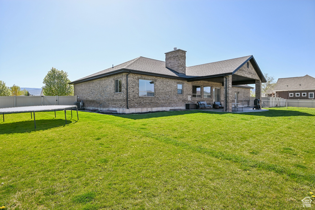 Back of house with a trampoline, brick siding, a chimney, a patio, and a shingled roof