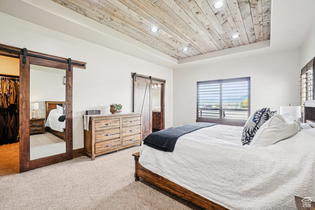Carpeted bedroom with a barn door, a raised ceiling, wood ceiling, recessed lighting, and a spacious closet