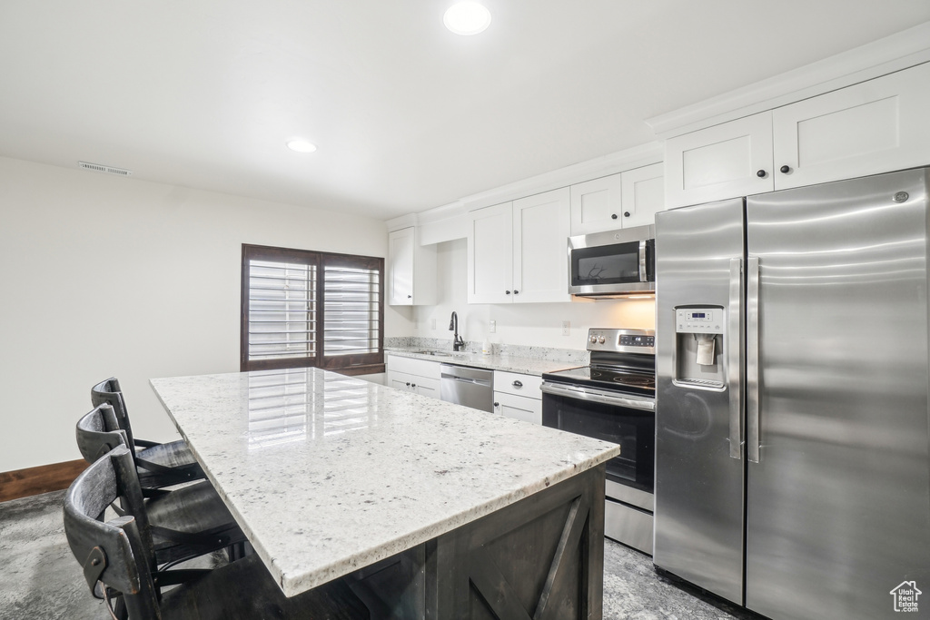 Kitchen featuring appliances with stainless steel finishes, white cabinets, a center island, a sink, and recessed lighting