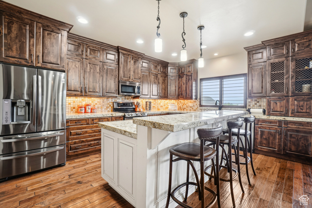 Kitchen featuring appliances with stainless steel finishes, a kitchen island, hardwood / wood-style floors, backsplash, and recessed lighting