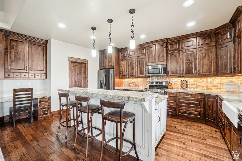 Kitchen with appliances with stainless steel finishes, dark wood-style flooring, tasteful backsplash, a center island, and a kitchen bar