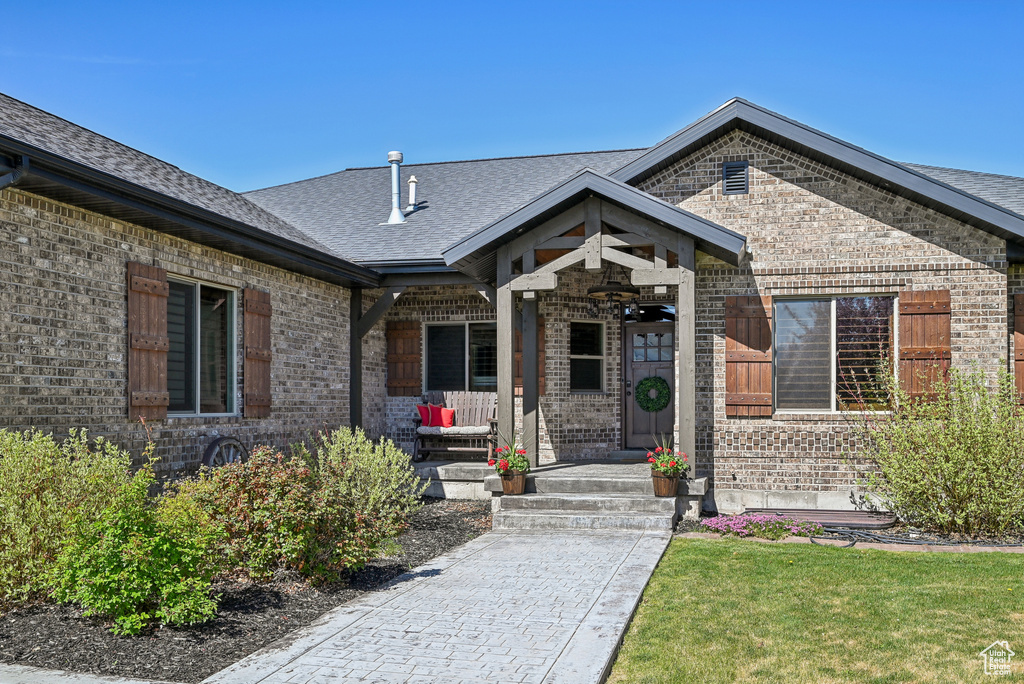 Property entrance with brick siding, covered porch, a shingled roof, and a yard