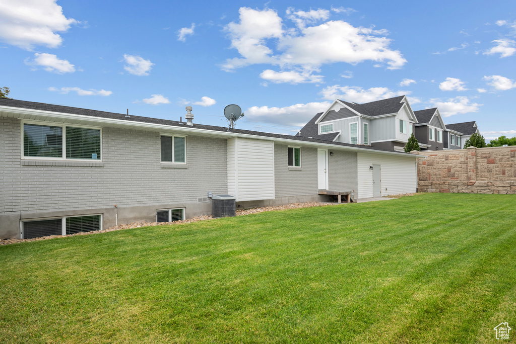 Back of house featuring central AC unit, a yard, and brick siding