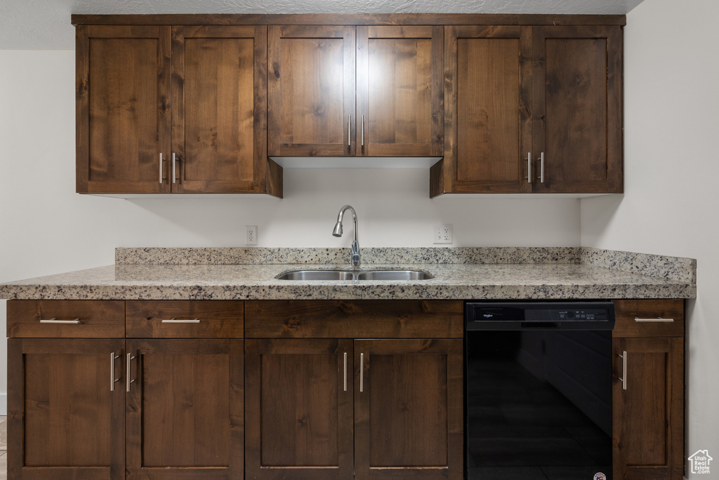 Kitchen featuring black dishwasher, a sink, light stone counters, and dark brown cabinets