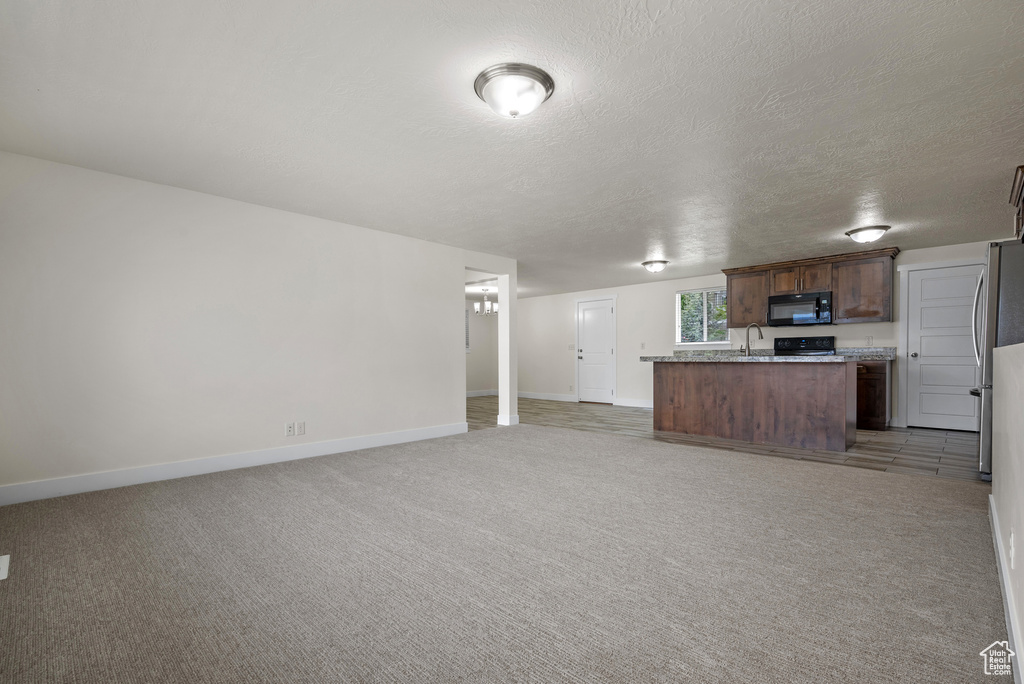 Unfurnished living room with a sink, baseboards, light colored carpet, and a textured ceiling