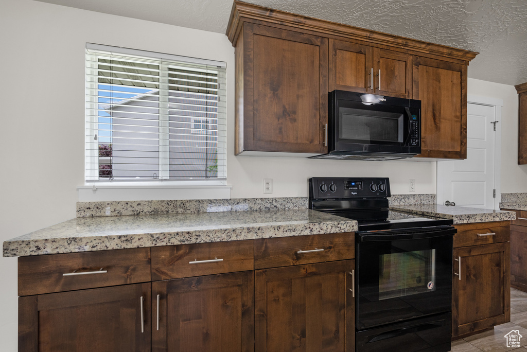 Kitchen featuring black appliances, a textured ceiling, and light stone counters