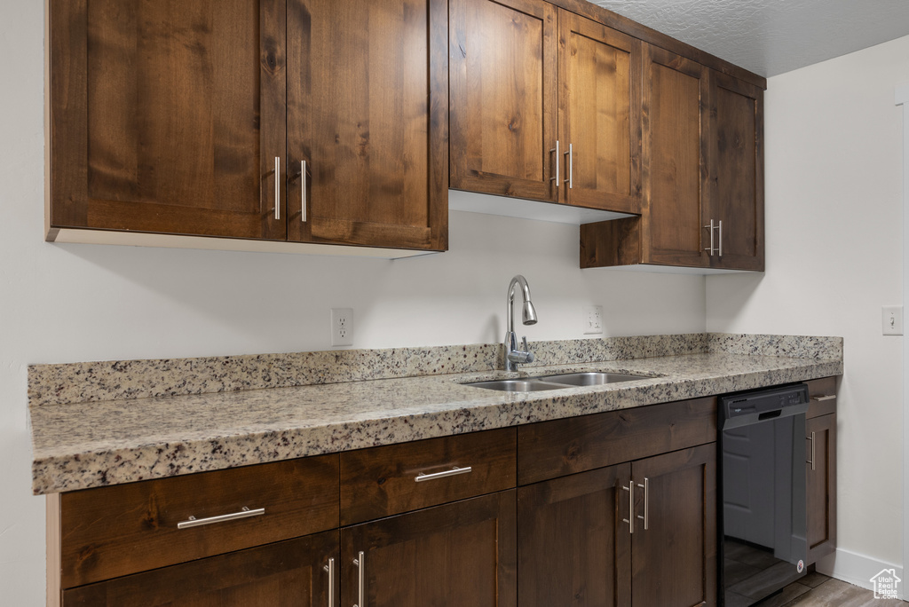 Kitchen with a sink, dishwasher, light stone countertops, and dark brown cabinets