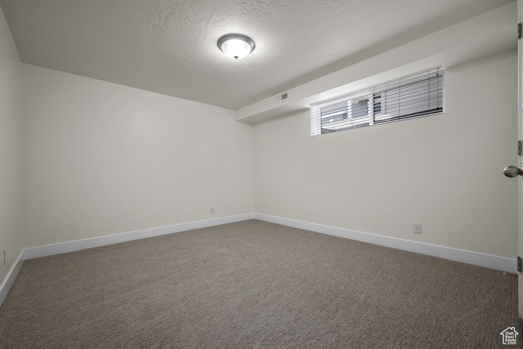 Carpeted spare room featuring a textured ceiling and baseboards