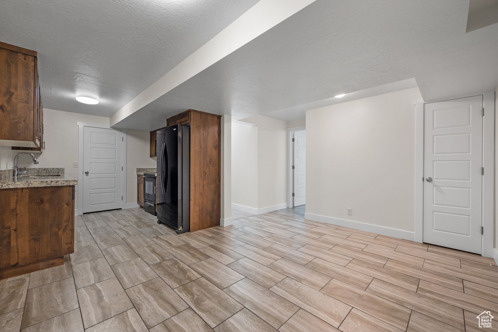 Kitchen with black appliances, a sink, baseboards, light stone counters, and a textured ceiling