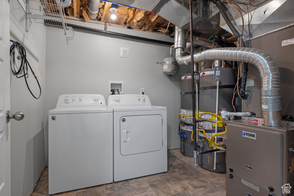 Washroom with washing machine and clothes dryer, water heater, and stone finish floors