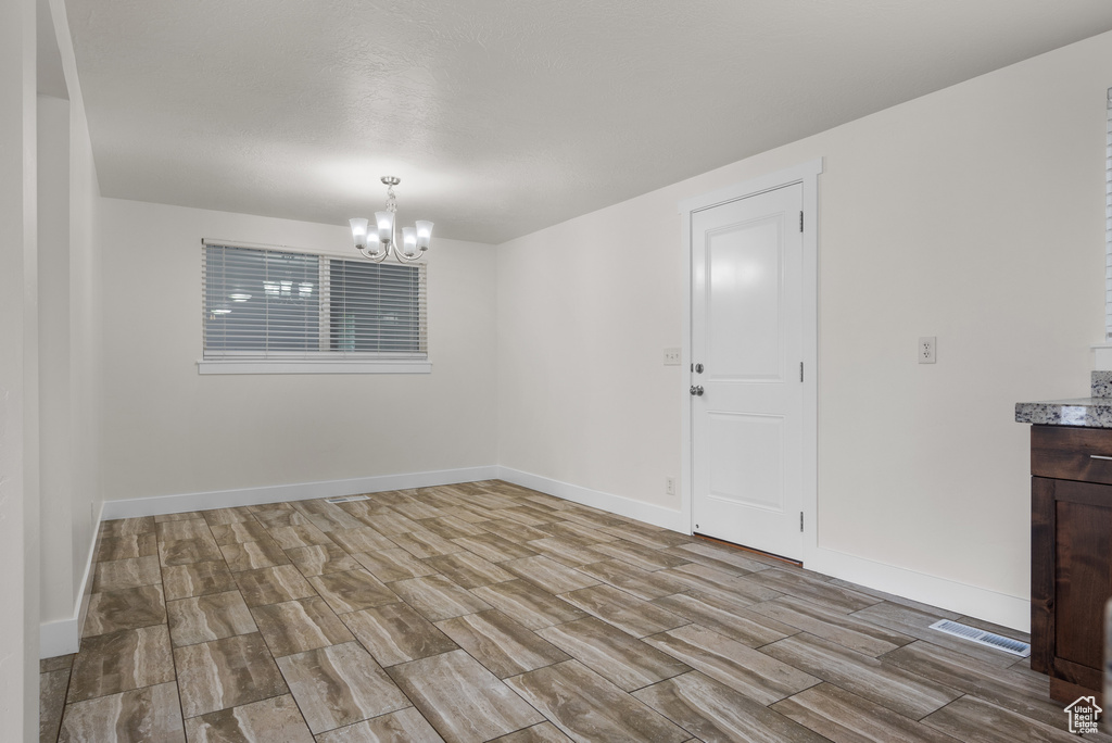 Unfurnished room with a chandelier, wood tiled floors, and baseboards