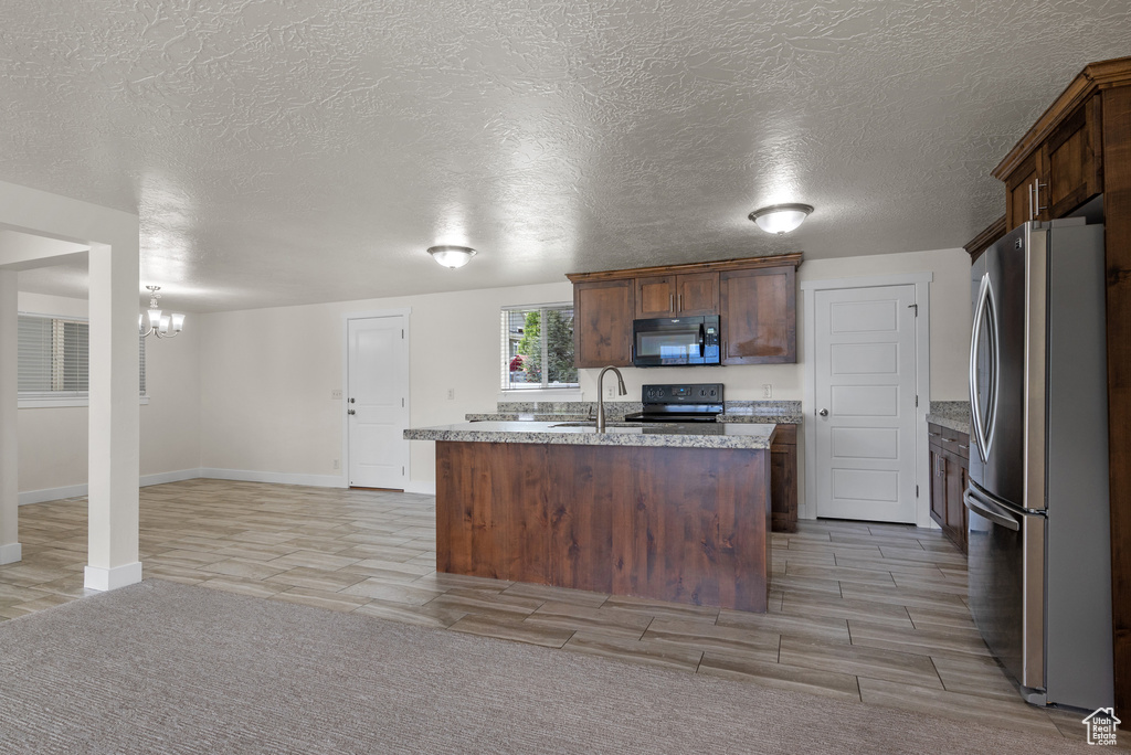 Kitchen featuring black appliances, a chandelier, a center island with sink, baseboards, and a sink