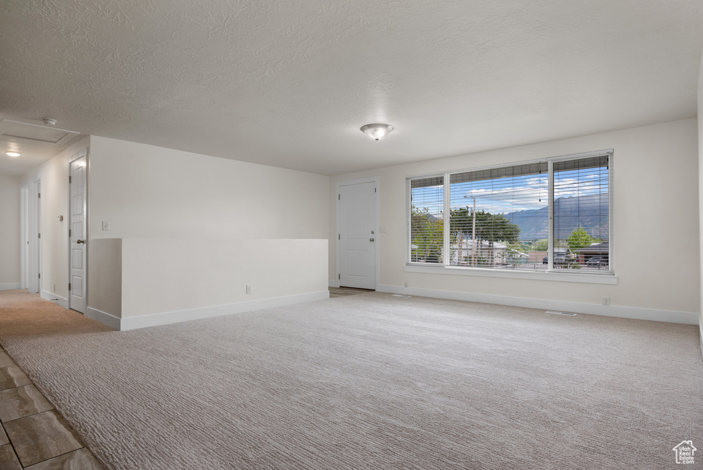 Empty room featuring attic access, a textured ceiling, baseboards, and light colored carpet