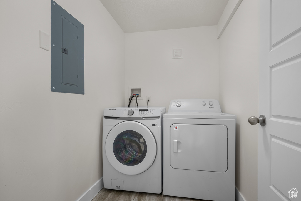Laundry room featuring electric panel, washer and dryer, baseboards, and wood finished floors