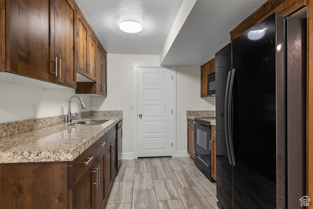 Kitchen with black appliances, a sink, baseboards, a textured ceiling, and wood finish floors