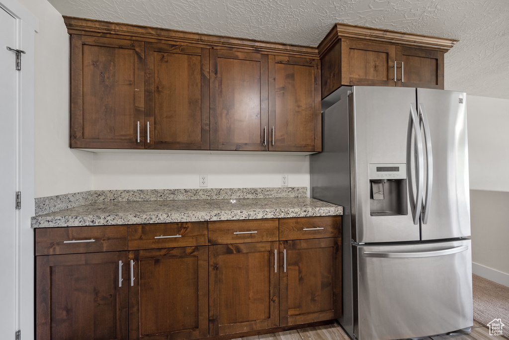 Kitchen featuring stainless steel fridge with ice dispenser, light stone counters, baseboards, and a textured ceiling