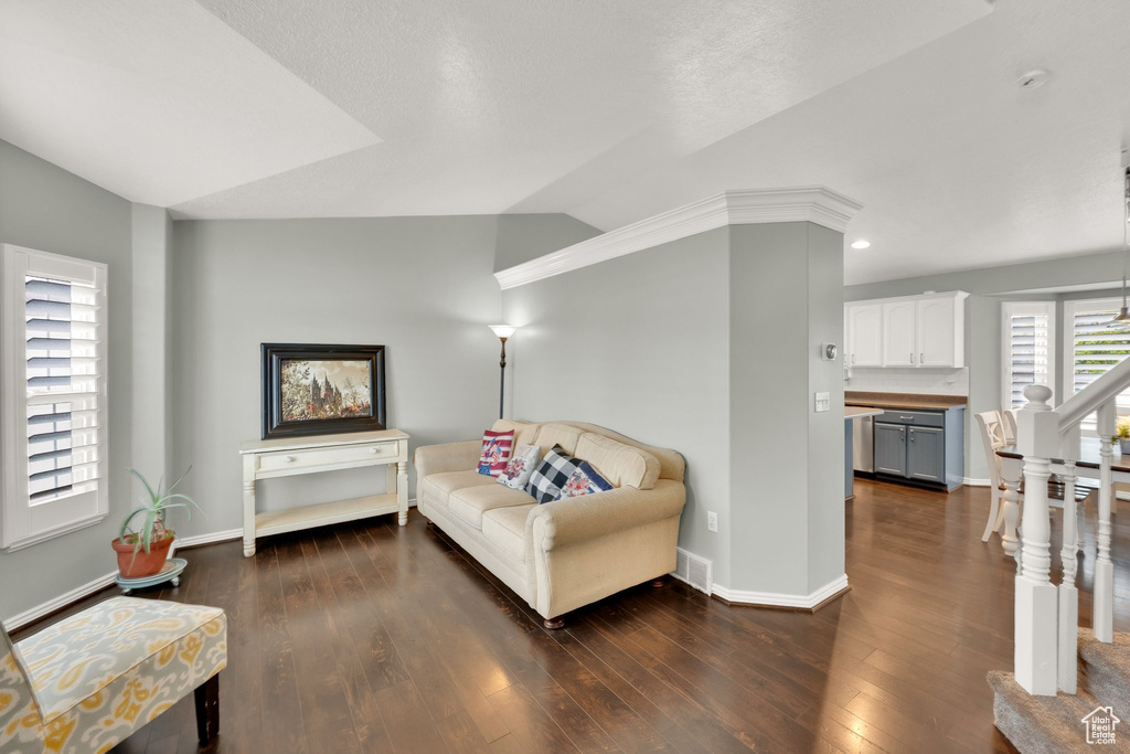 Living room featuring dark wood-type flooring, baseboards, vaulted ceiling, and stairway