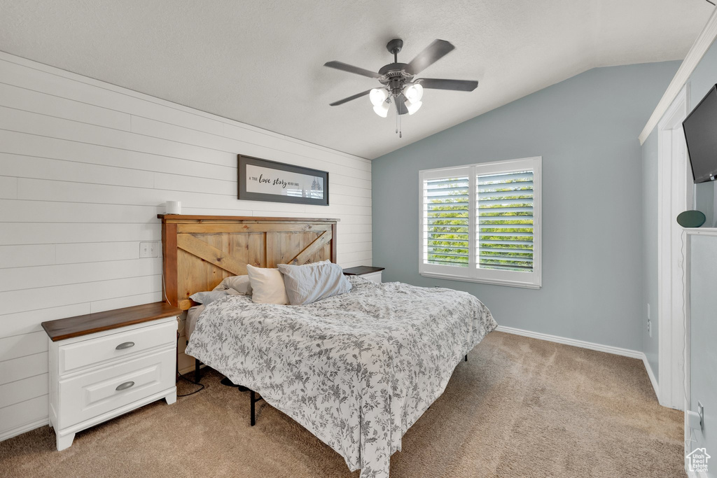 Bedroom with light carpet, vaulted ceiling, a ceiling fan, wood walls, and baseboards