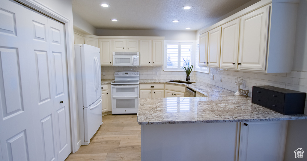Kitchen with white appliances, a peninsula, recessed lighting, light wood-style flooring, and decorative backsplash
