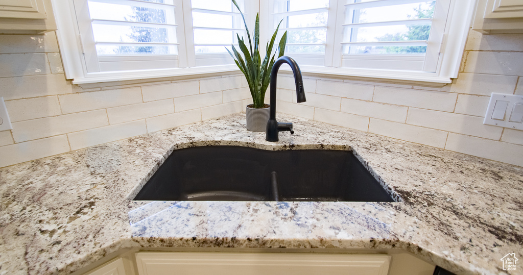 Kitchen view of a sink, backsplash, light stone countertops, and white cabinets