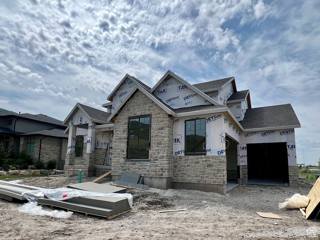 Property under construction with stone siding, roof with shingles, and a garage