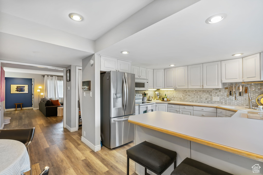 Kitchen featuring white appliances, baseboards, a peninsula, backsplash, and recessed lighting