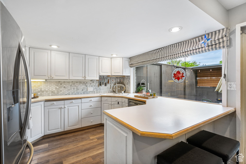 Kitchen with stainless steel fridge, a peninsula, dark wood-type flooring, white cabinets, and decorative backsplash