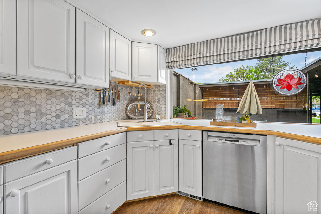 Kitchen featuring stainless steel dishwasher, a sink, white cabinetry, and decorative backsplash