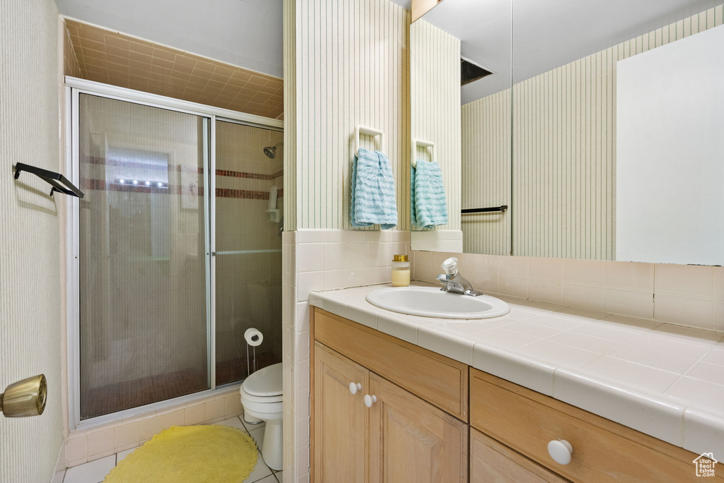 Bathroom with toilet, a shower stall, vanity, tile patterned flooring, and wallpapered walls