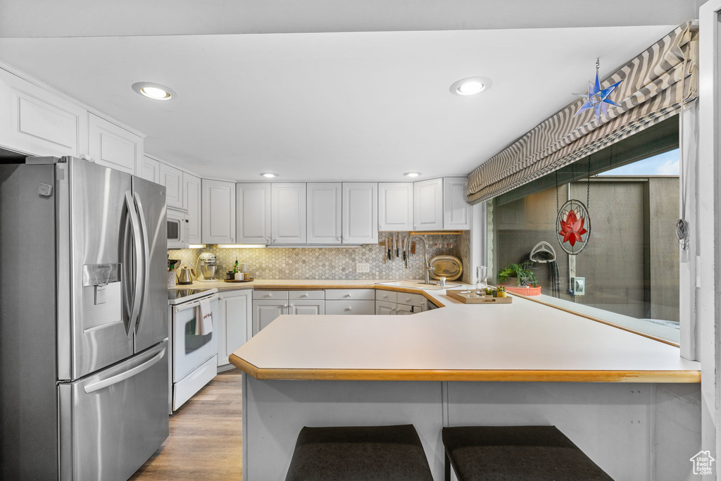 Kitchen with white appliances, a peninsula, light countertops, backsplash, and white cabinetry