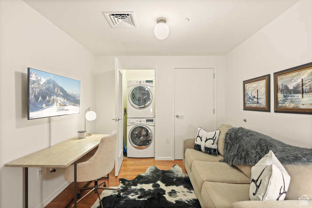 Washroom featuring stacked washer / dryer, wood finished floors, and a desk